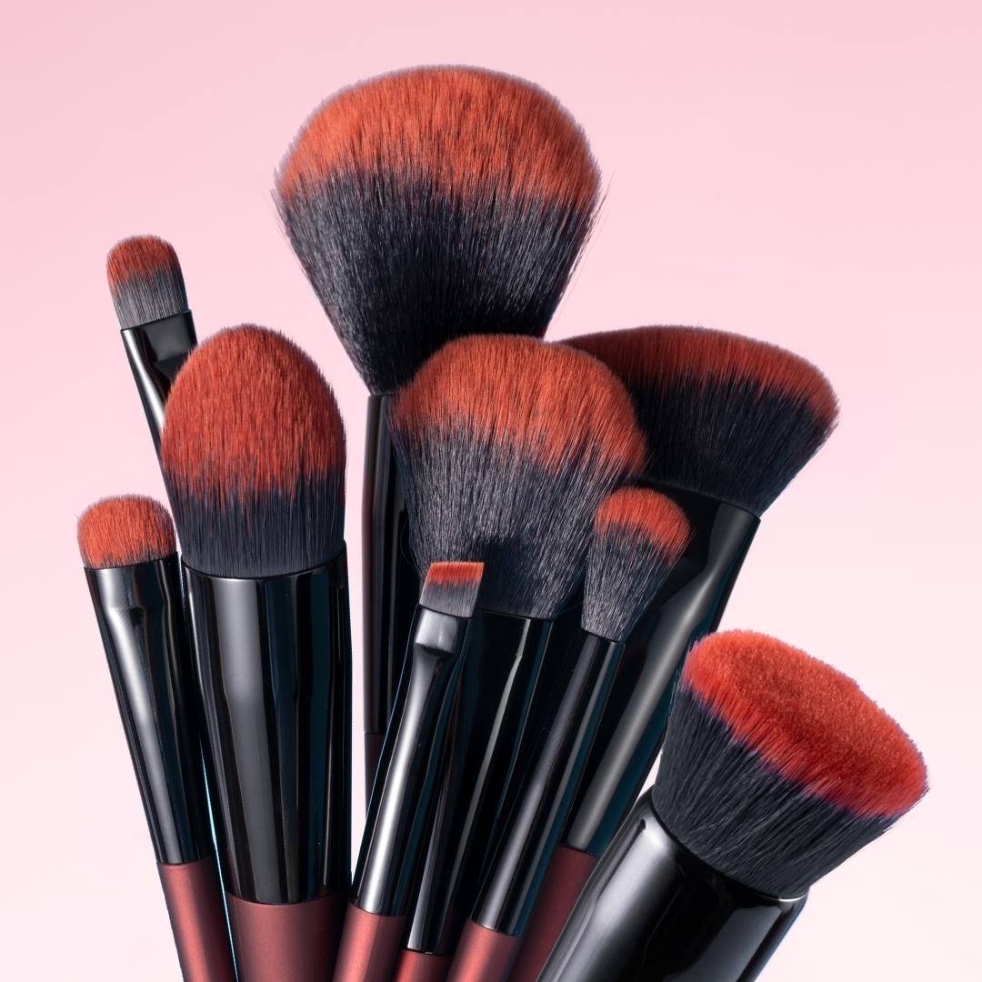 Aria Pro 12-piece makeup brush set featuring soft red and black bristles with sleek handles against a pink background.