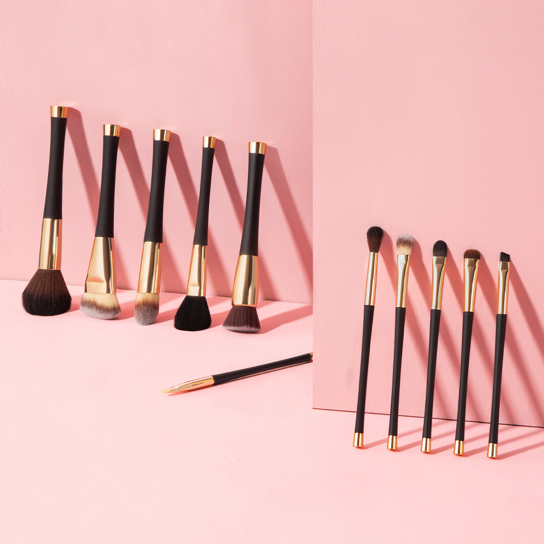 Aria Pro 12-piece makeup brush set with black handles and gold ferrules displayed on a soft pink background.
