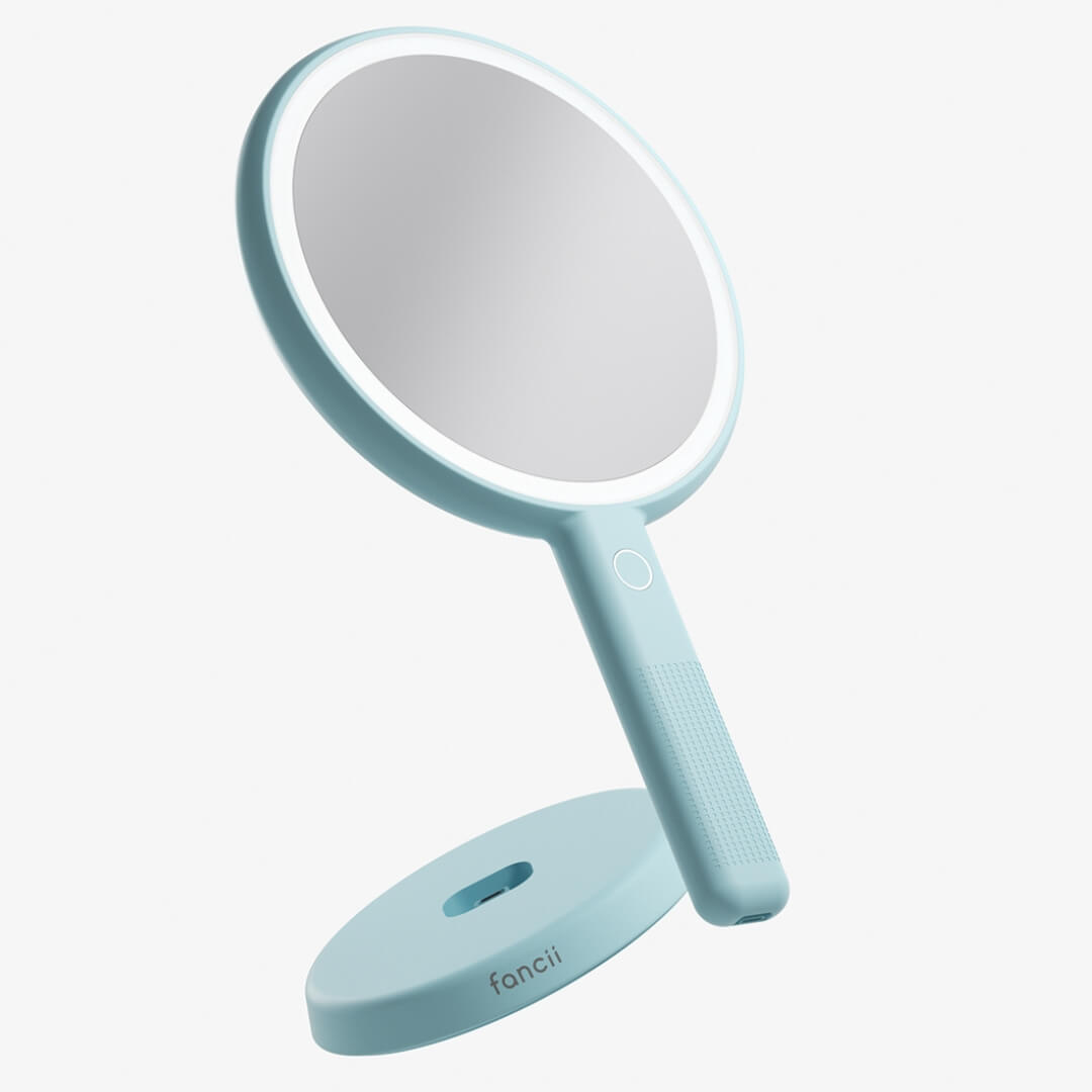 Light blue Cami LED lighted handheld makeup mirror on its vanity base with 1x/5x magnification ring light.