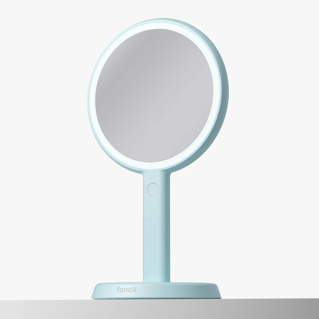 Cami light blue 2-in-1 LED lighted handheld makeup mirror with 1x/5x magnification on a matching vanity stand.