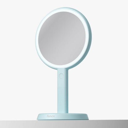 Cami light blue 2-in-1 LED lighted handheld makeup mirror with 1x/5x magnification on a matching vanity stand.