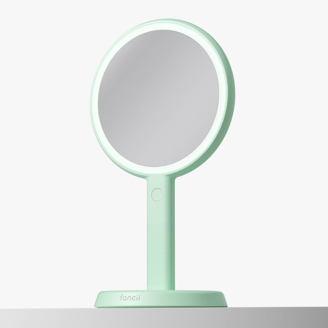 Cami mint green LED lighted handheld makeup mirror with 1x/5x magnification on a matching vanity stand.