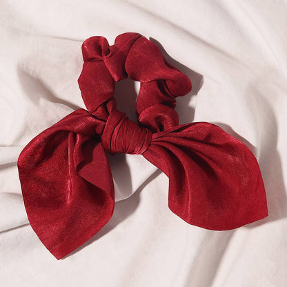Elle red satin scrunchie with bow detail on a white fabric background.