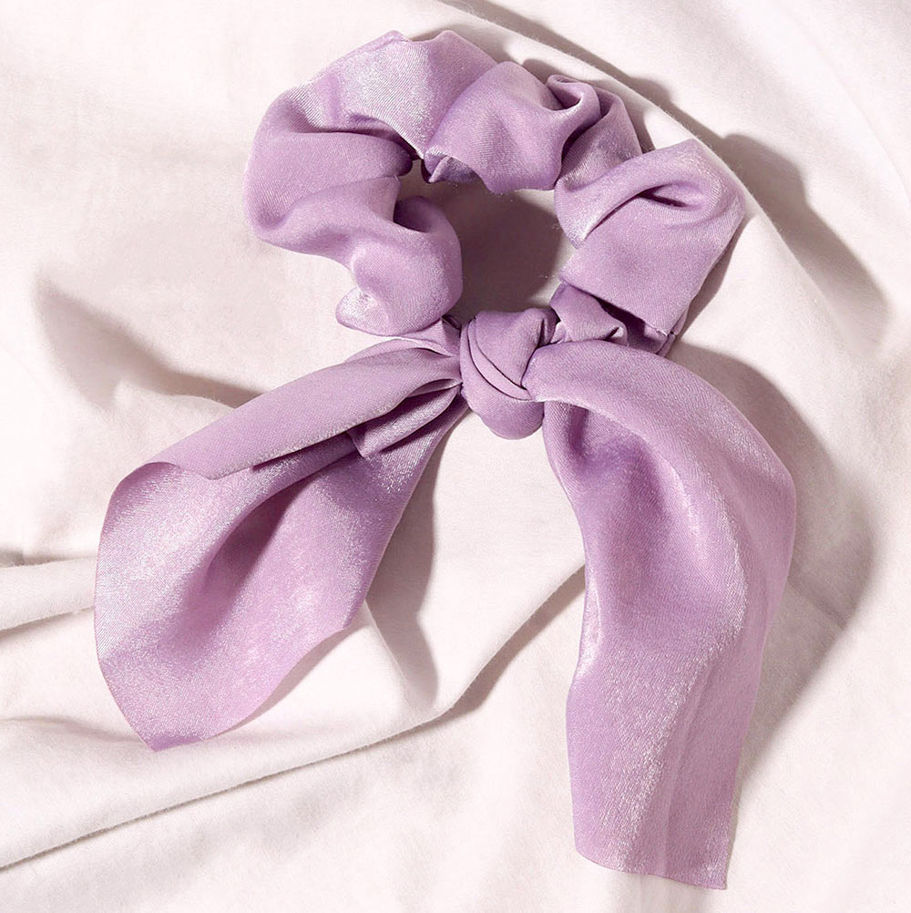 Elle light purple lavender satin scrunchie with chic bow detail on soft white textured fabric background.