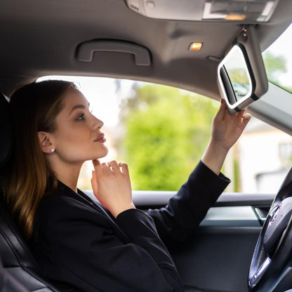 Woman using Juni 2 LED lighted car visor mirror for makeup in a vehicle, showcasing portable travel vanity lighting.