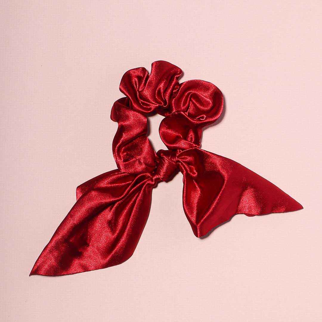 Elle red satin scrunchie with a decorative chic bow accessory for hair styling, displayed on a pink background.