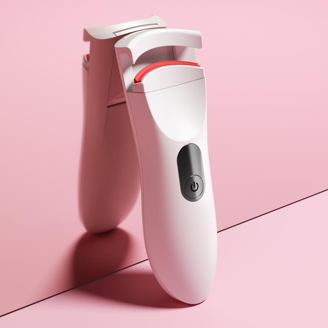 White Tasha Heated Eyelash Curler with red silicone pad and power button on a soft pink background.