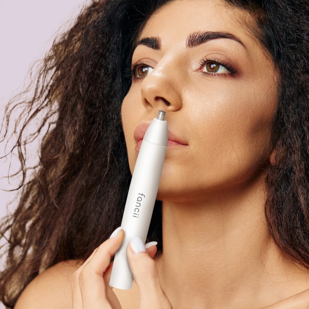 Woman using Torri painless nose hair trimmer with precision dual-edge blades for facial grooming and smooth skin.