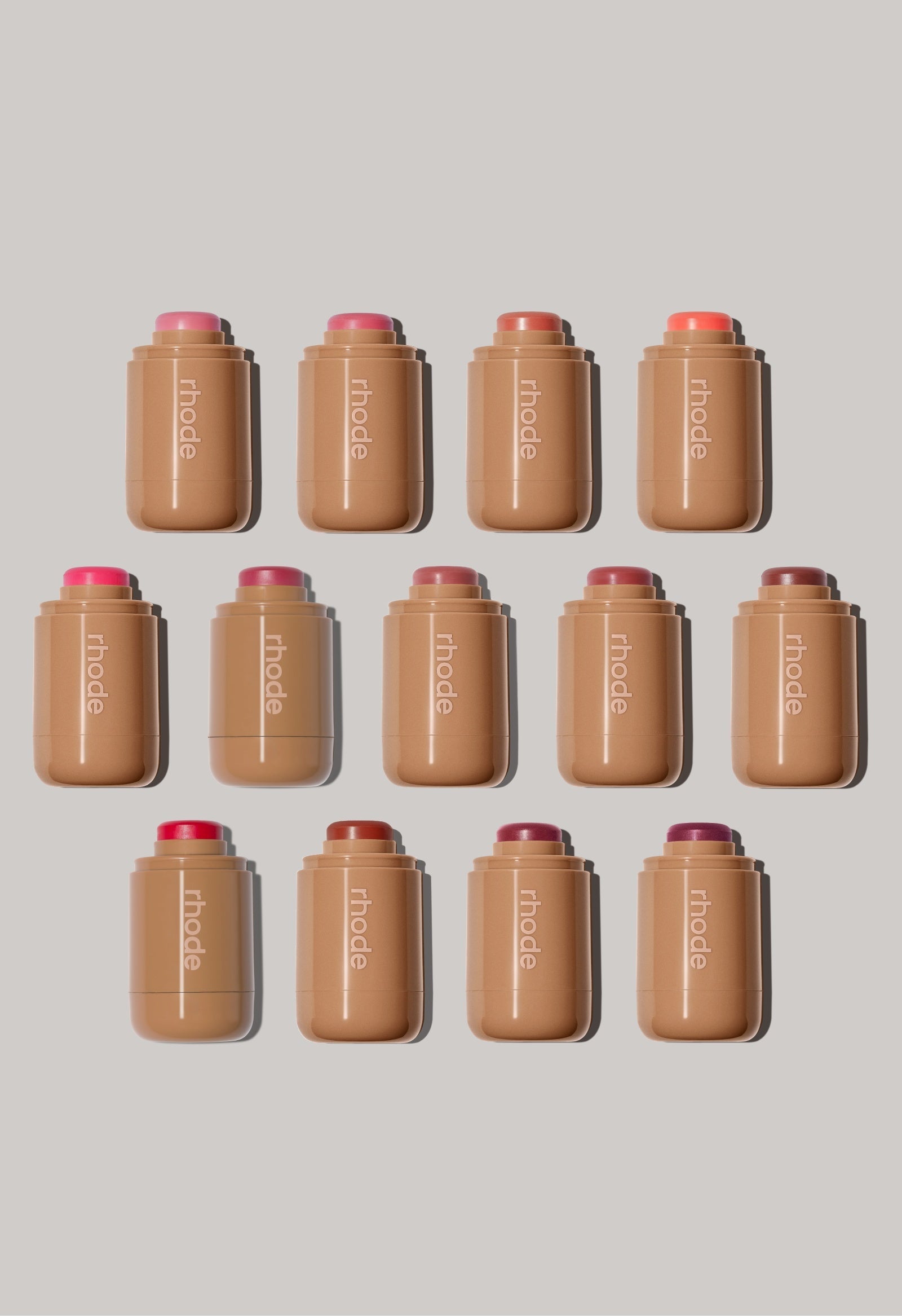 A collection of Rhode Pocket Blush cream makeup sticks in 13 dewy shades ranging from soft pinks to deep berry tones.