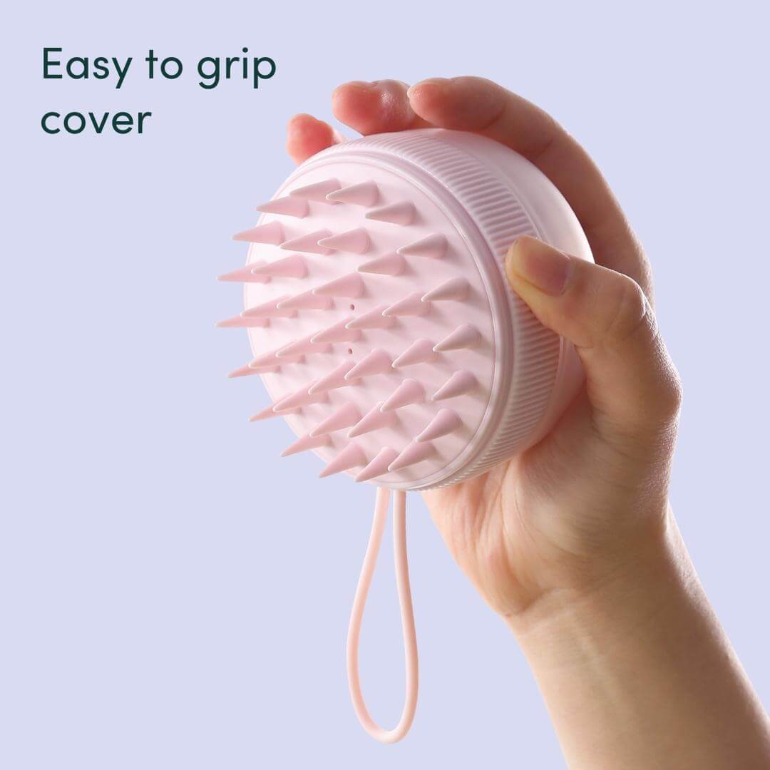 Hand holding a pink Charlotte silicone scalp massager brush with easy-grip cover and soft bristles for exfoliating.