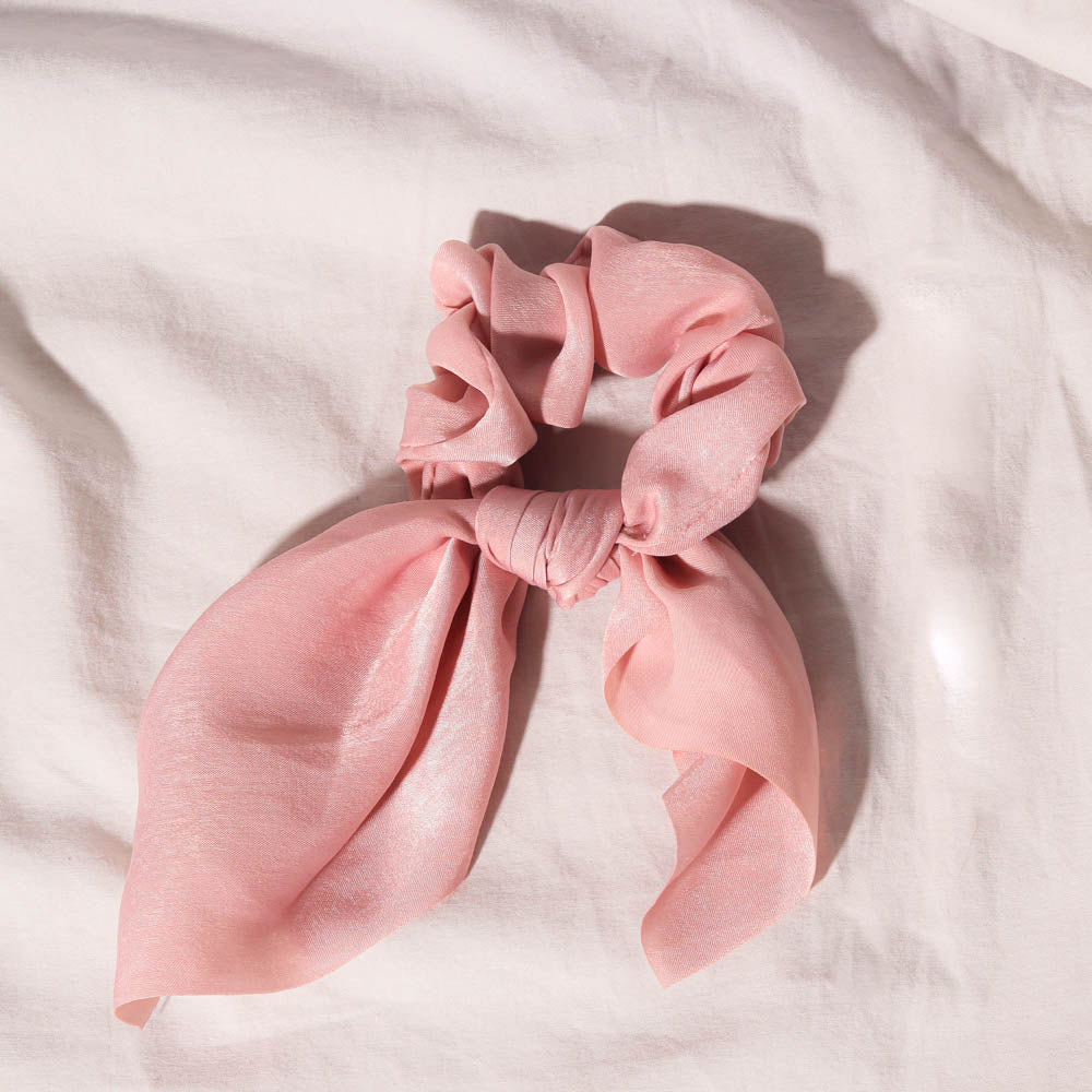 Elle pink satin hair scrunchie with a chic bow tie detail on a soft textured fabric background.