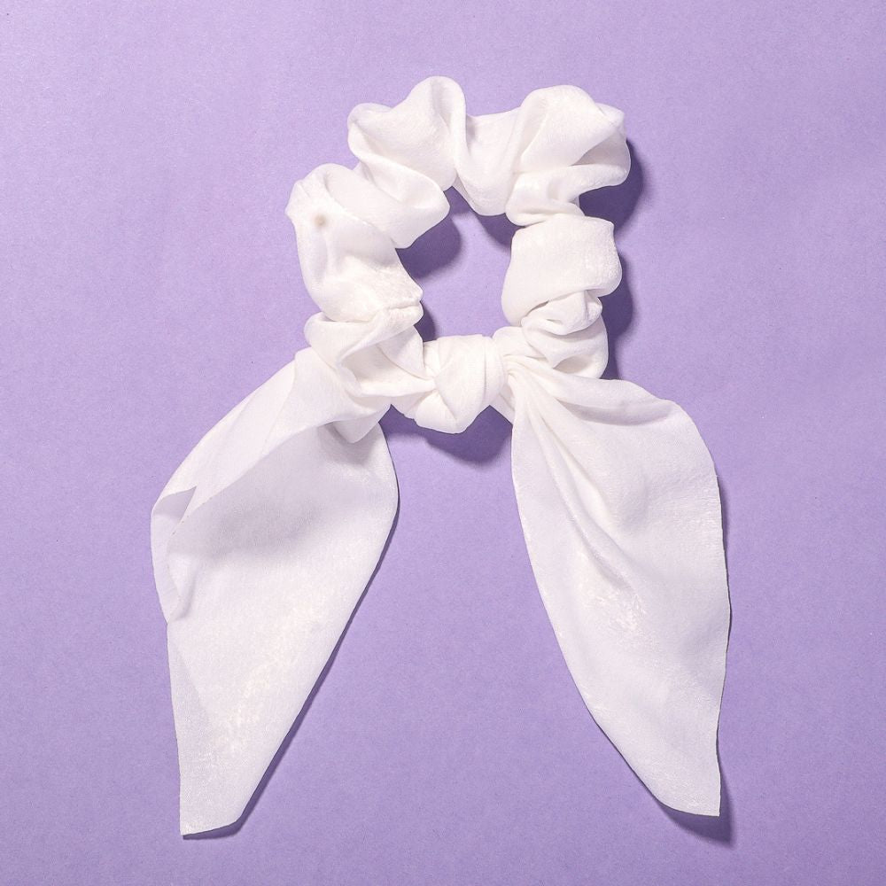 Elle white satin scrunchie with chic bow detail on a purple background.
